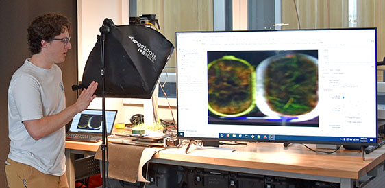 a man explains what is seen on a large computer monitor as the SUSHI scans pots of vegetation
