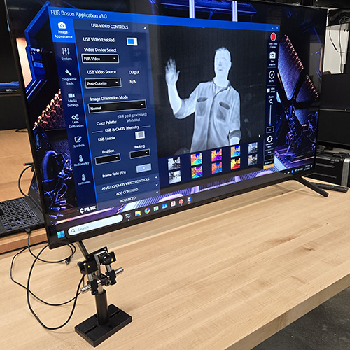 the small thermal imager sits on a table and is connected to a monitor which displays a thermal image