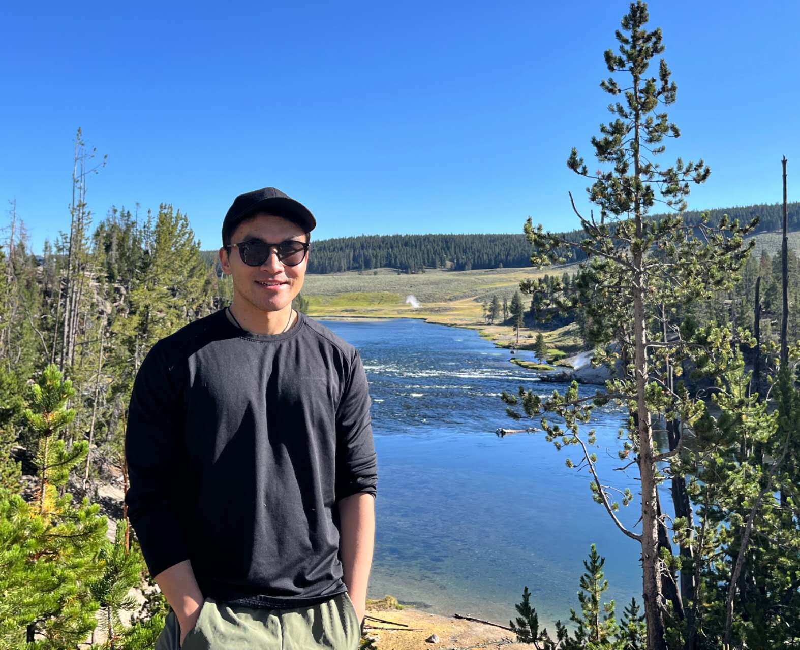 Lixu Jin at Yellowstone NP with a lake and trees in the background