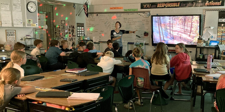 an instructor shows a video on a classroom monitor as students observe the images of a prescribed fire