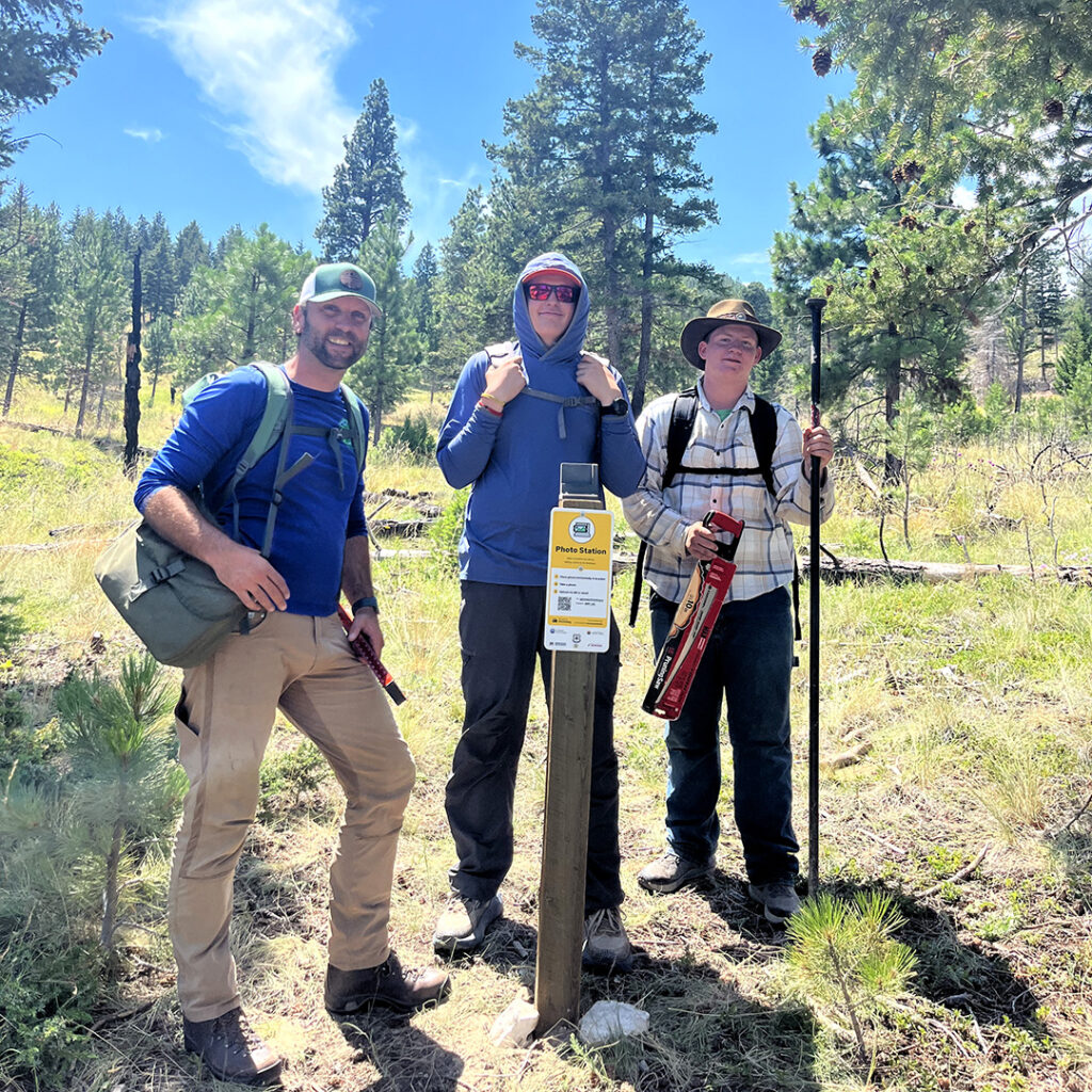 three men stand in a forest with a newly installed Chronolog sign