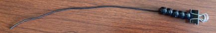 Black elastic cord with binder clip at one end and five black beads strung on it