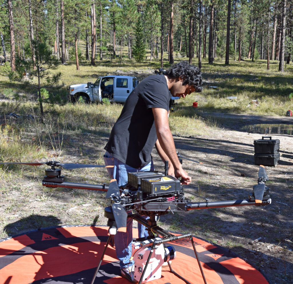 a man adjusts a drone on its landing pad in a forest setting