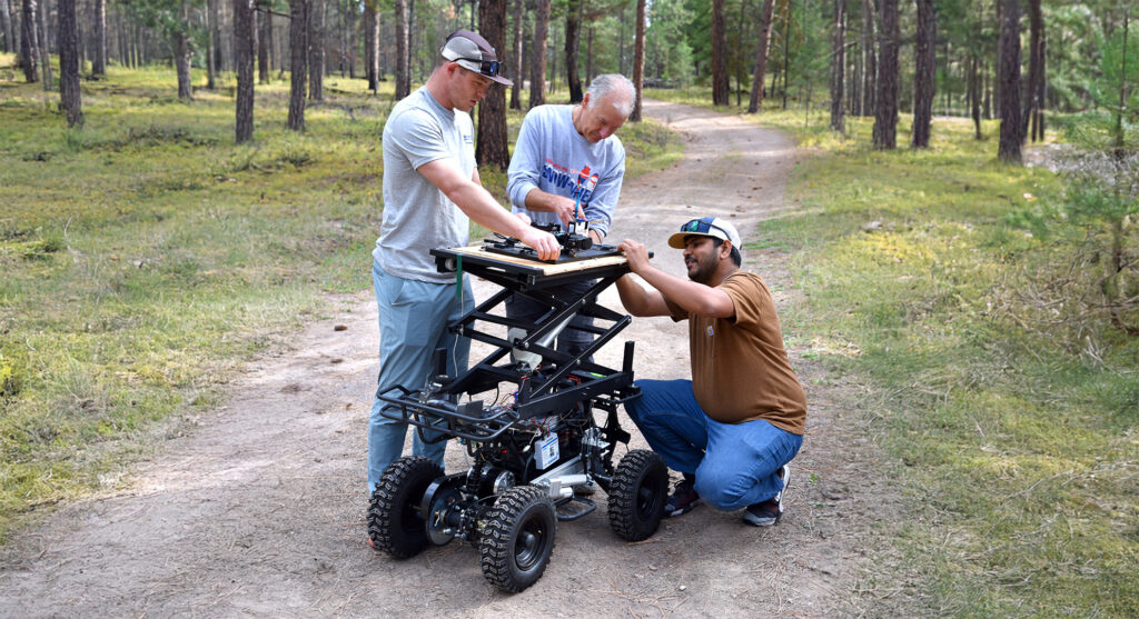 Three men working on a ground rover in a forest